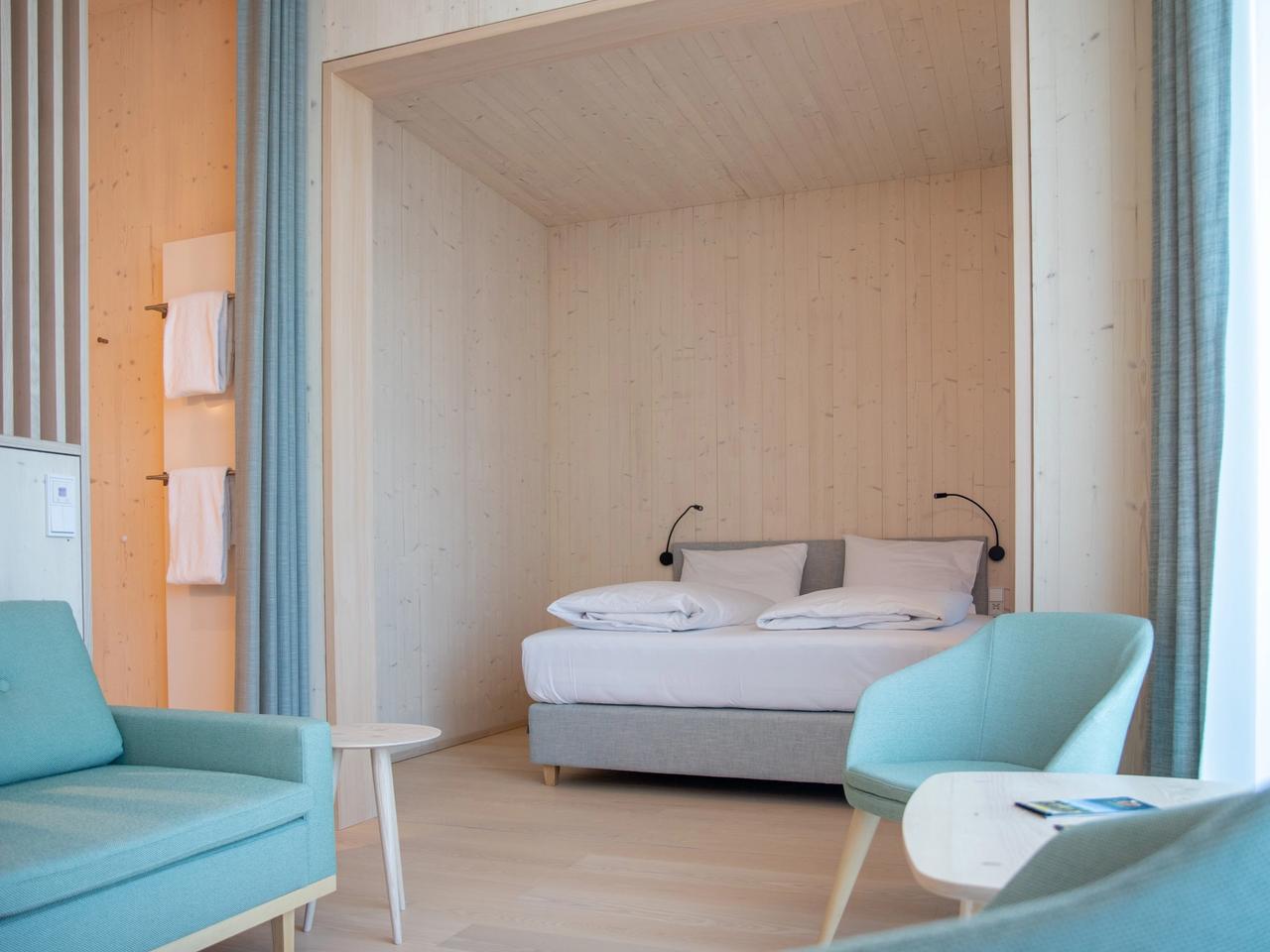 Hotelzimmer mit Schlafnische aus hellem Holz und türkisen Sesseln
