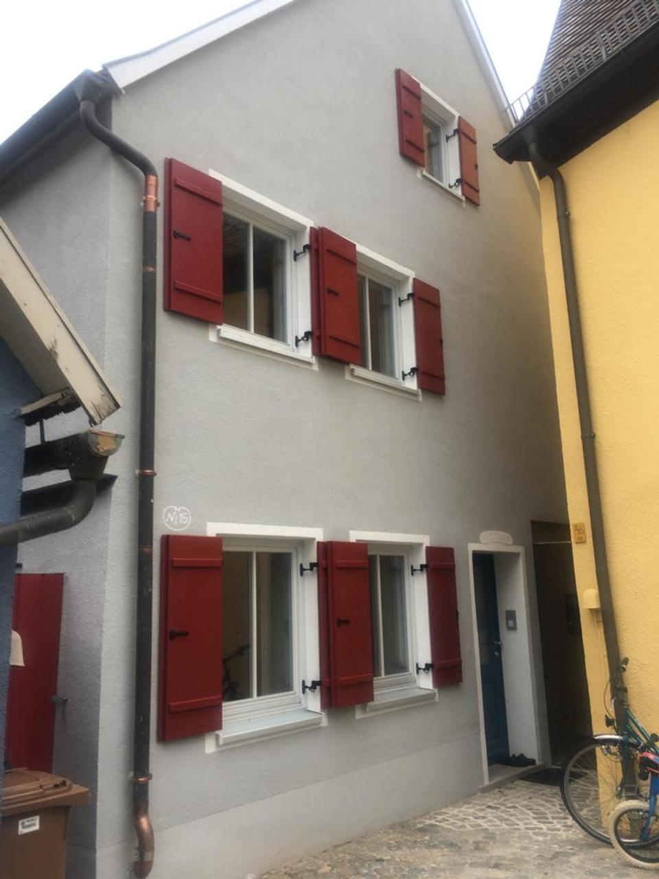 Sanierte Stadthaus-Fassade mit grauem Putz und roten Fensterläden