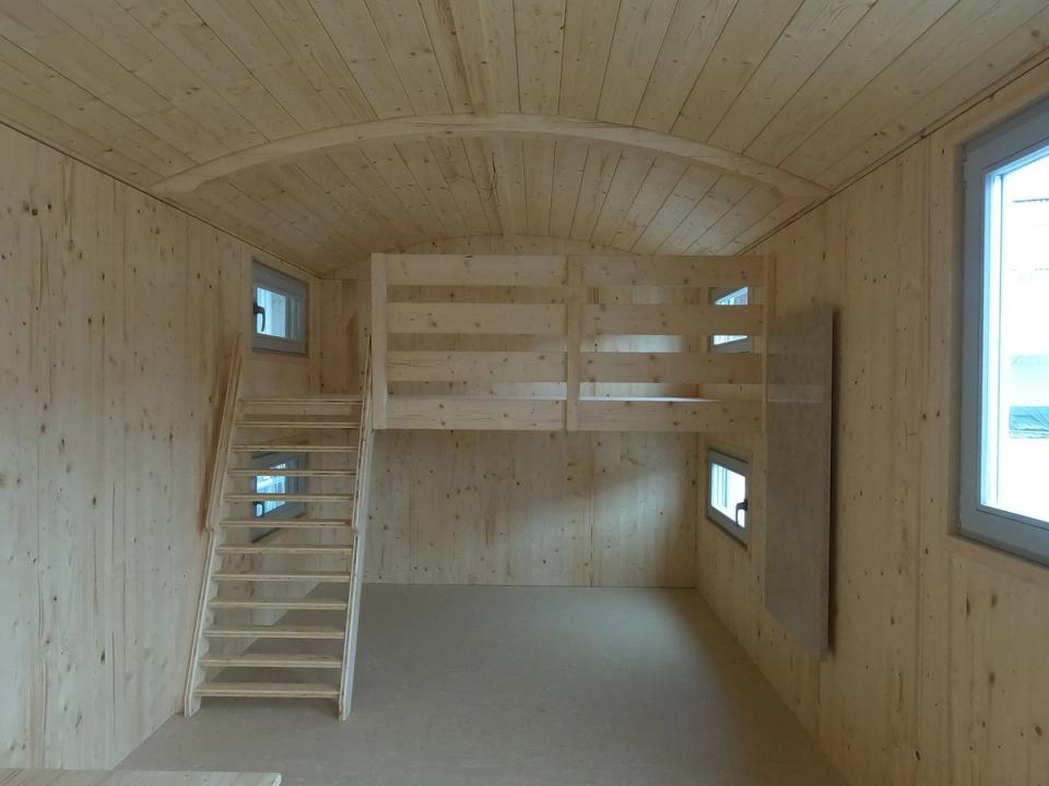 Innenraum aus hellem Holz mit Hochebene und steiler Holztreppe unter dem gewölbten Dach