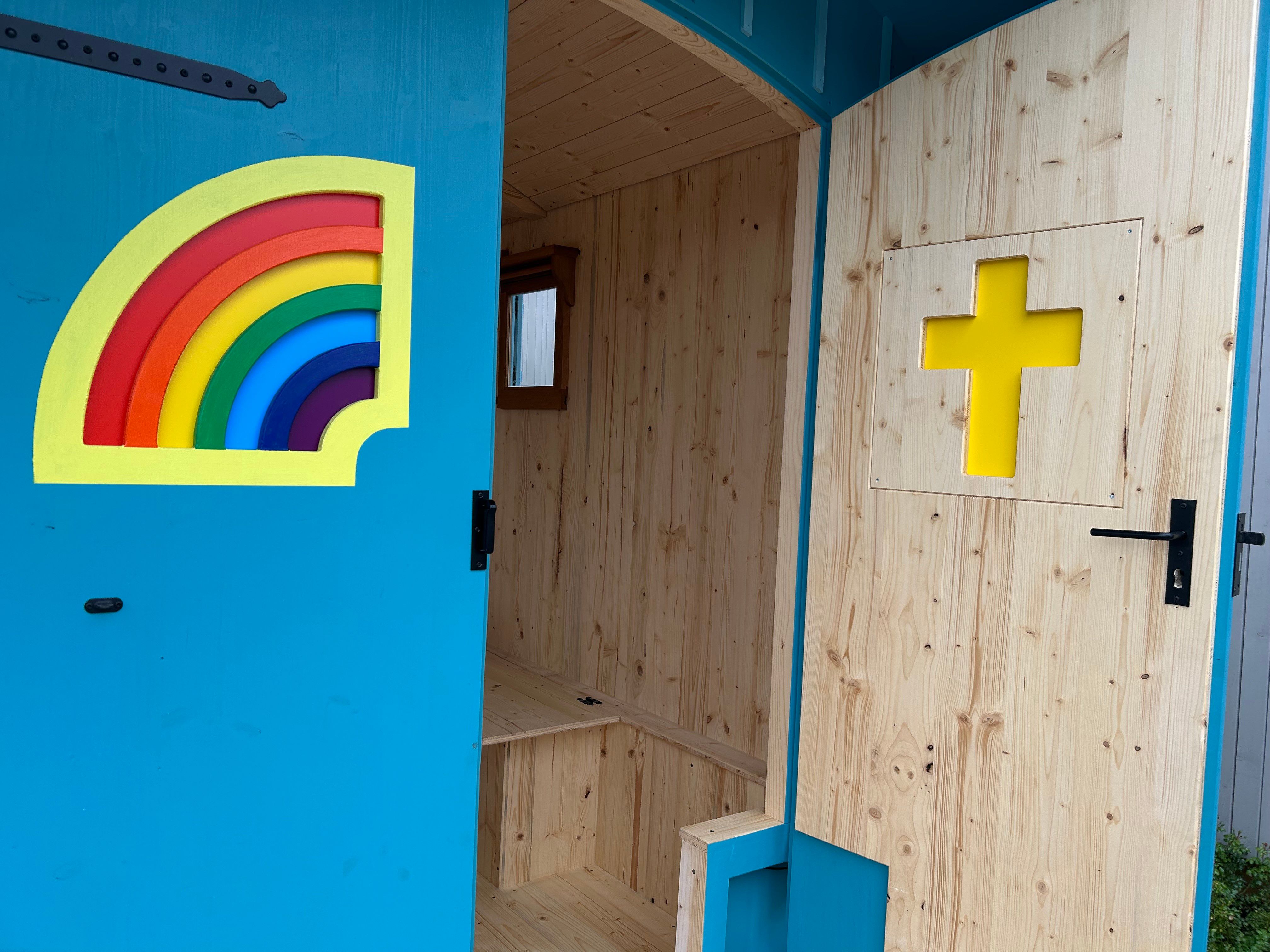 Tür des Kirchenwagens mit Regenbogenfenster und gelbem Kreuz, Blick in den hellen Innenraum