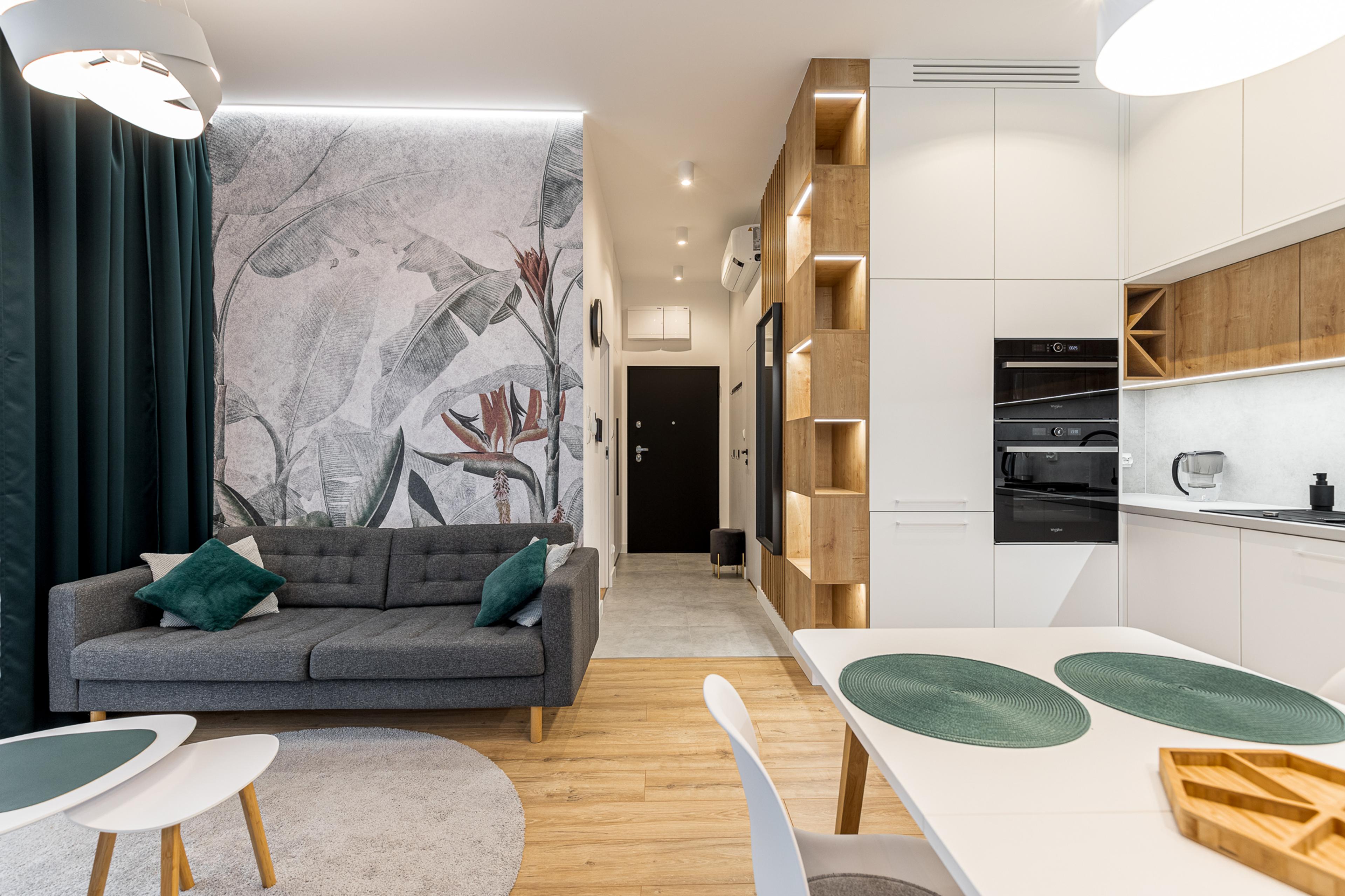 Apartamento moderno à venda em Wrocław – sala de estar elegante com papel de parede de design, detalhes em madeira e cozinha integrada. Investimento ideal em imóveis premium.