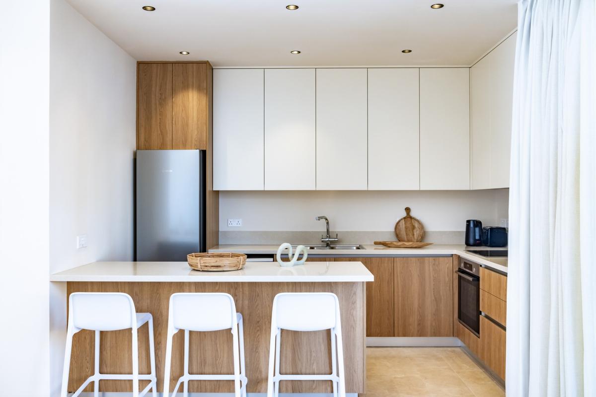 Cucina moderna e luminosa con penisola, mobili bianchi e frontali in legno — interno di un appartamento a Cipro