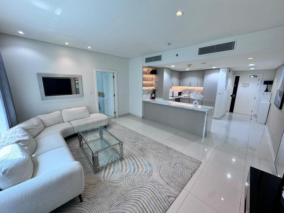 Avoin pohjaratkaisu Palm Jumeirah -asunnossa: olohuone kulmasohvalla, koristeellinen matto ja keittiö marmori-saarekkeella