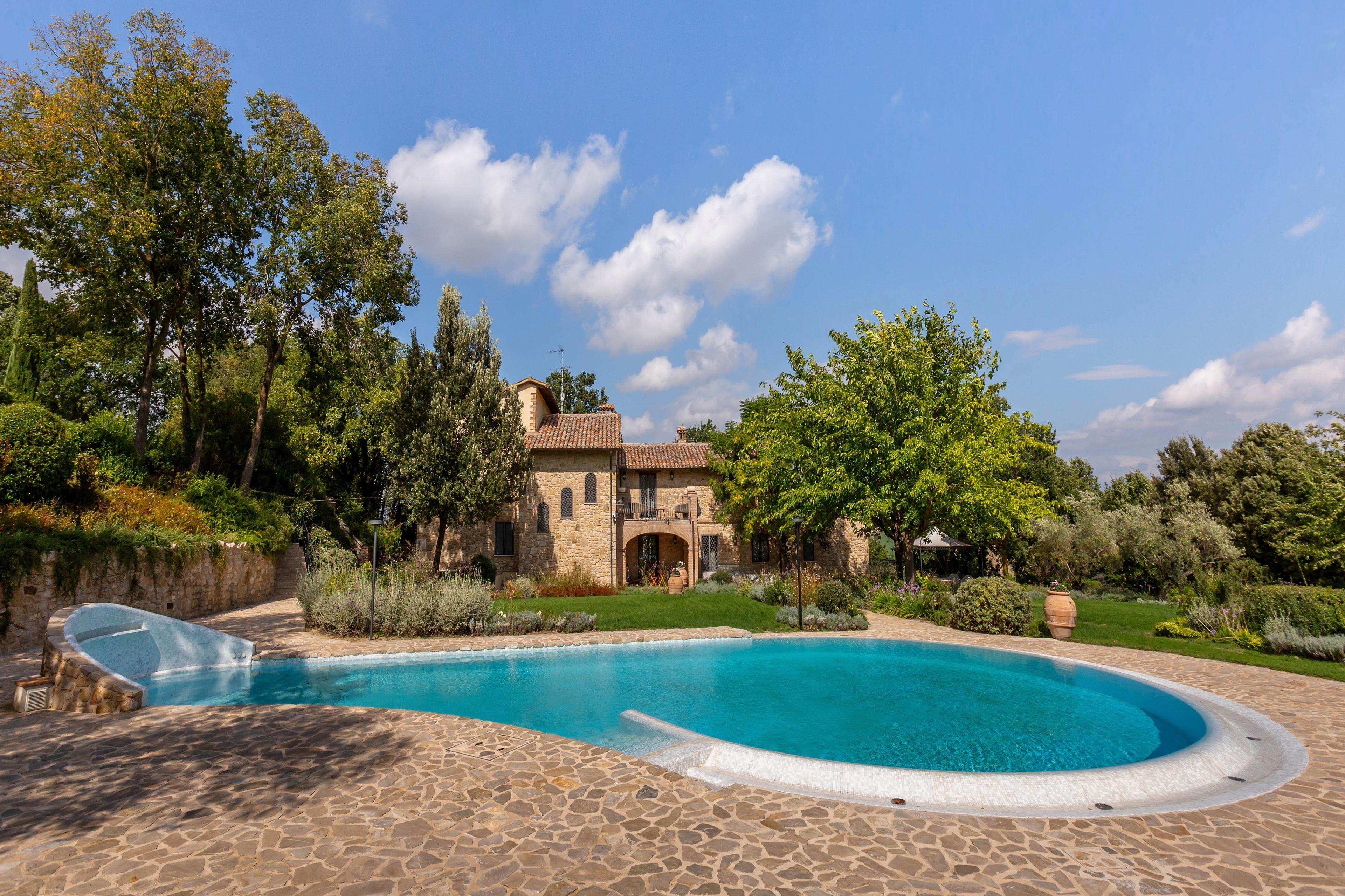 Villa con piscina in vendita in Umbria, circondata da giardino e alberi, proprietà vacanze ideale in Italia con vista sulle colline.