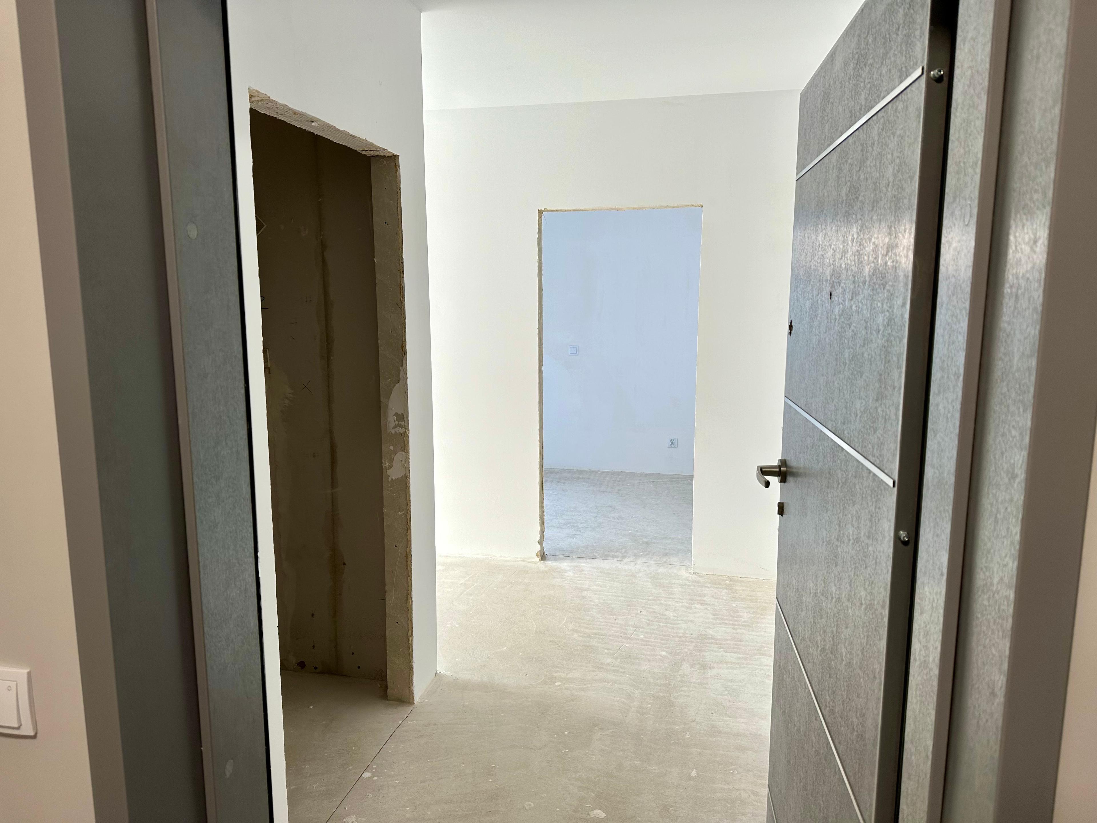 Nouvel appartement en état de développement | Intérieur à aménager | Couloir spacieux dans l'appartement. Finition développeur avec des murs blancs et un sol en béton. État brut fermé avec portes intérieures installées. Appartement moderne dans un immeuble résidentiel avec installations prêtes. Propriété prête pour un aménagement personnalisé et une finition clé en main. Appartement lumineux avec potentiel d'investissement | Excellente localisation.