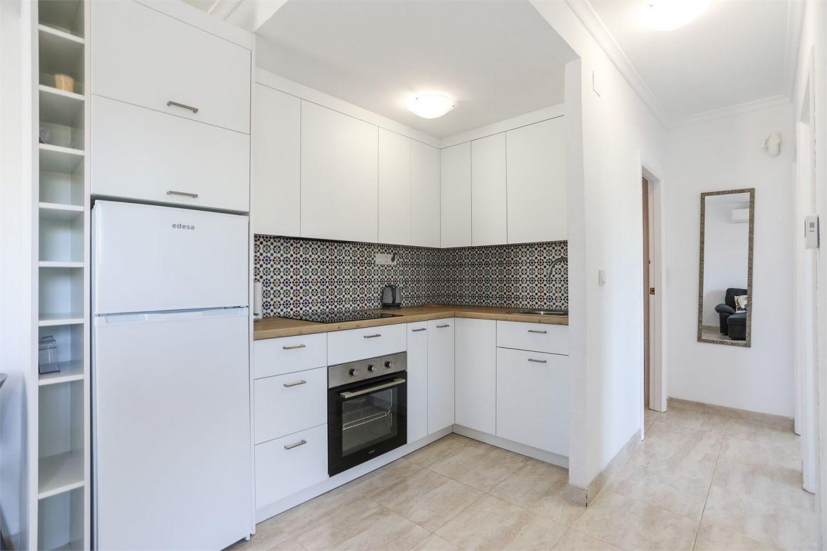 Weiße Küche in einer Wohnung an der Costa Blanca mit Backofen, Kühlschrank und dekorativer Mosaikfliese über der Arbeitsplatte