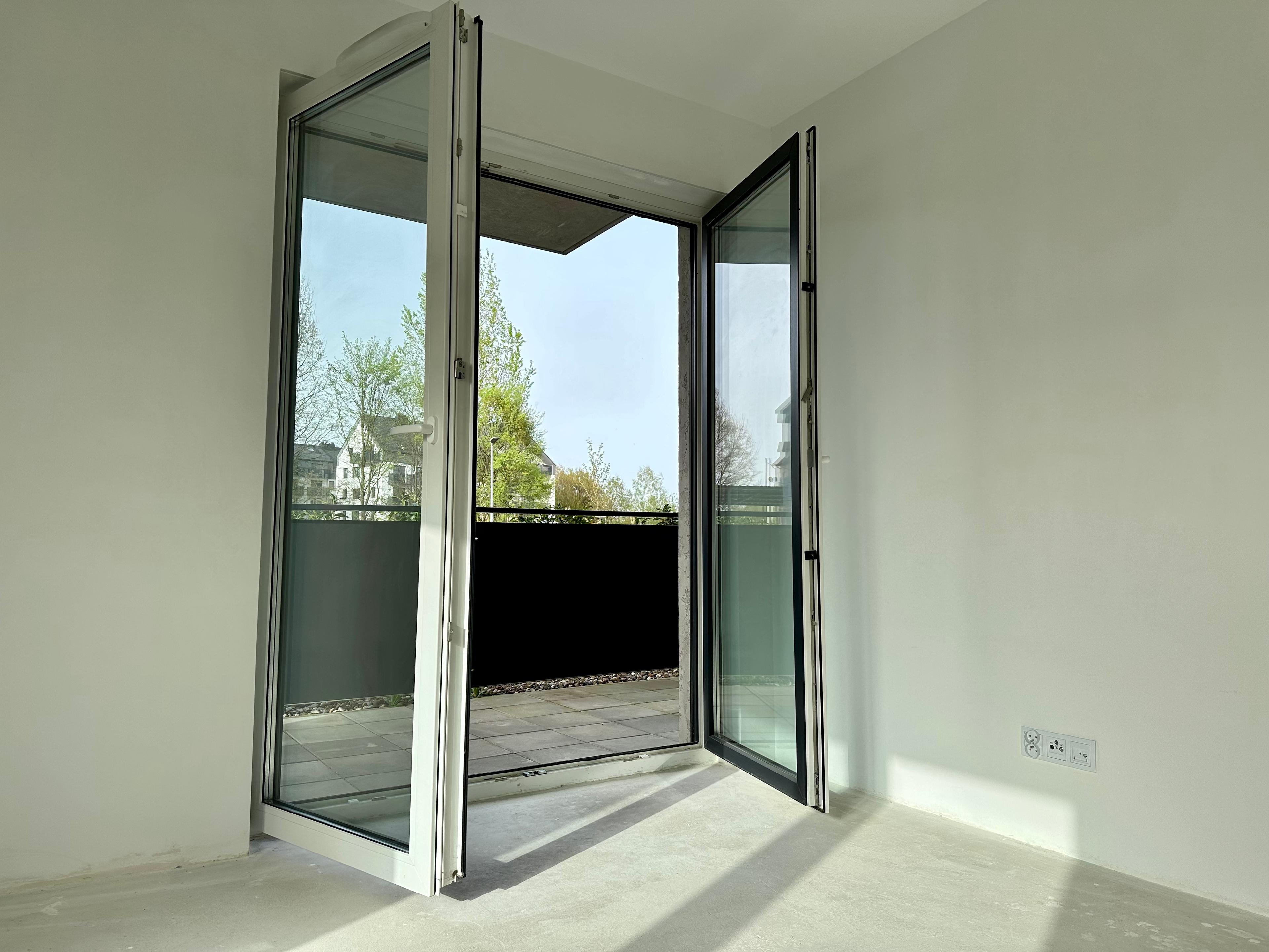 Appartement moderne avec balcon spacieux – portes-fenêtres ouvertes laissant entrer beaucoup de lumière naturelle dans l'intérieur. Vue sur un quartier verdoyant et bâtiments modernes. Endroit idéal pour se détendre en plein air.