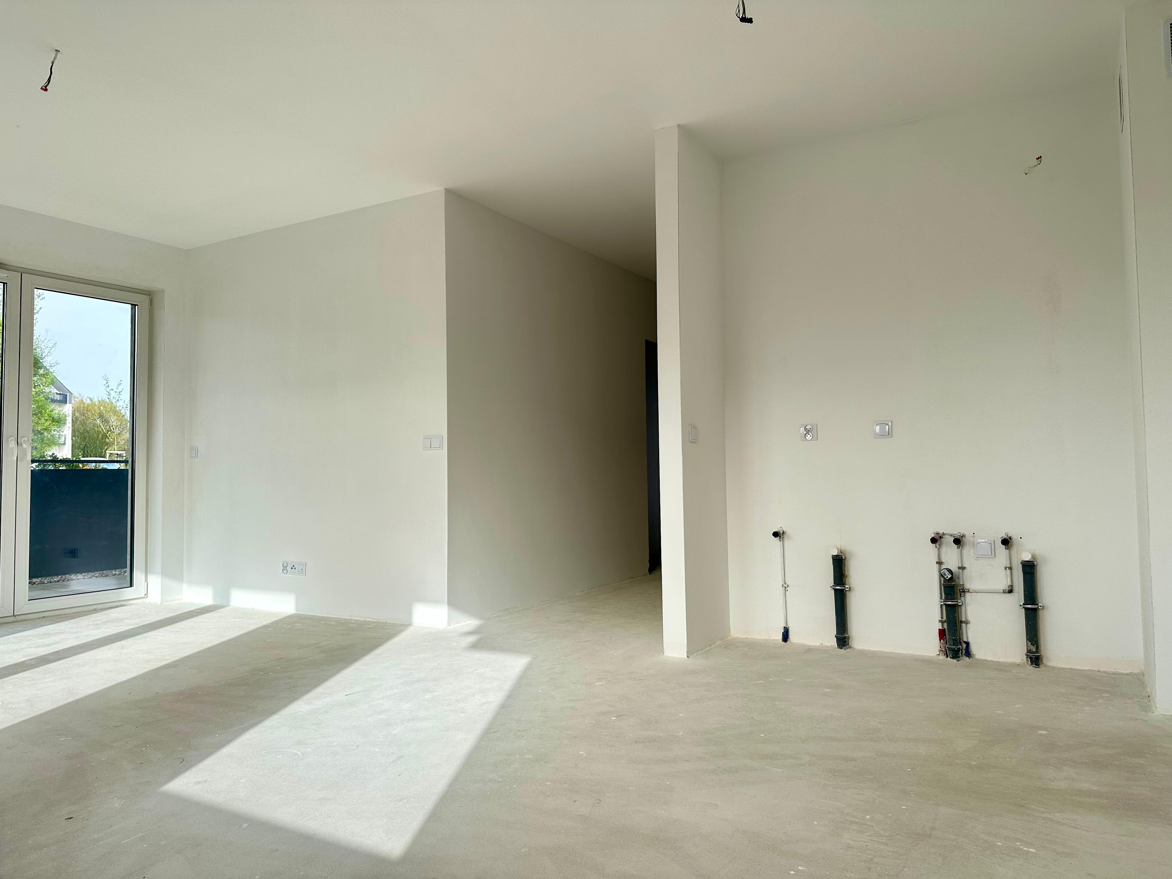 Nouvel appartement en état de développement – salon spacieux avec kitchenette et sortie sur balcon. Installations d'eau et d'égout prêtes pour l'installation de la cuisine. Intérieur lumineux avec beaucoup de lumière naturelle, idéal pour l'aménagement.