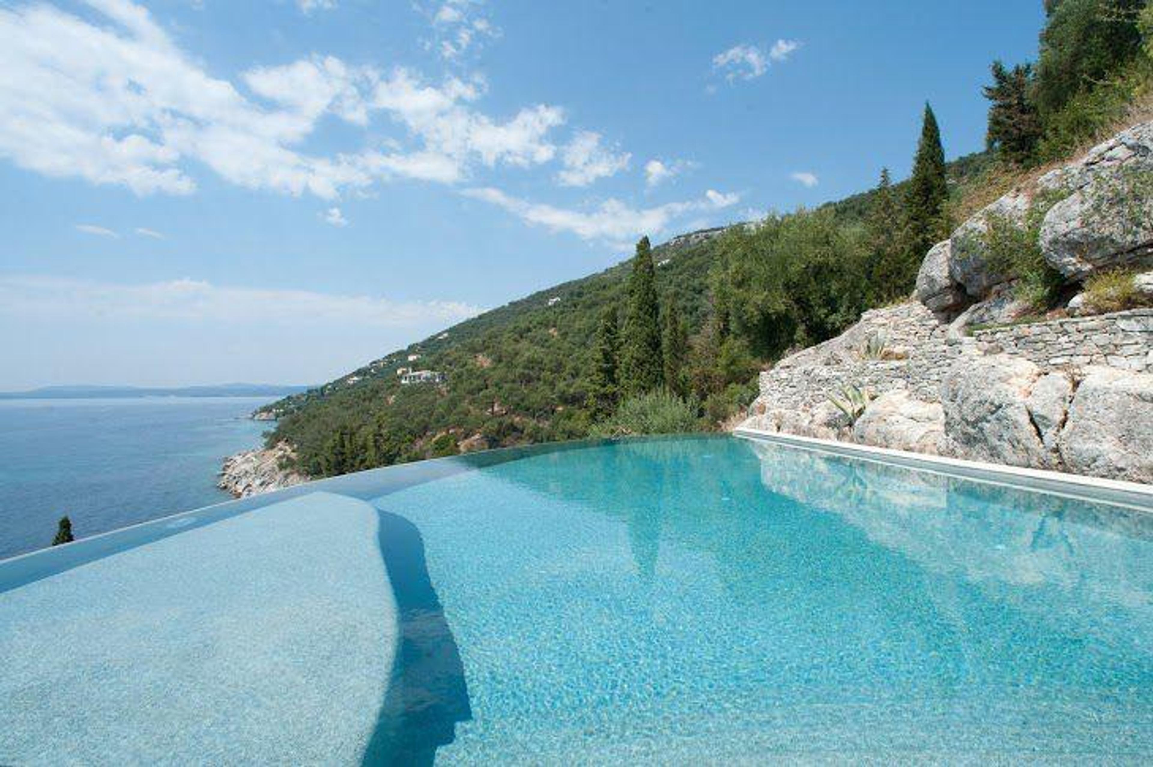 Infinity-pool på en grekisk ö – perfekt integrerad i naturligt stenlandskap, representerar de bästa grekiska öarna för investeringar i hus vid havet Grekland för programmet golden visa Grekland fastigheter med utsikt över det oändliga blå Egeiska havet.