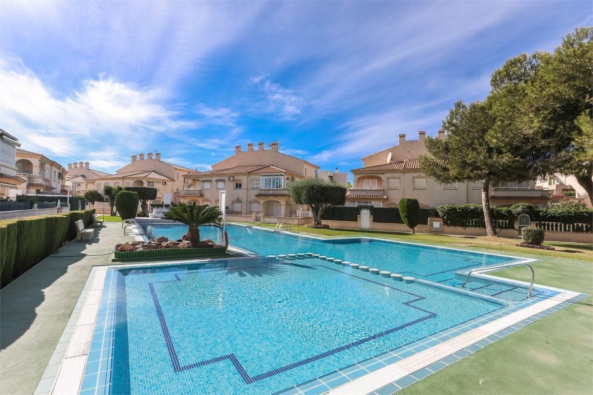 Gemeinschaftspool einer Wohnanlage an der Costa Blanca vor Reihenhäusern, mit gepflegter Bepflanzung und blauem Himmel