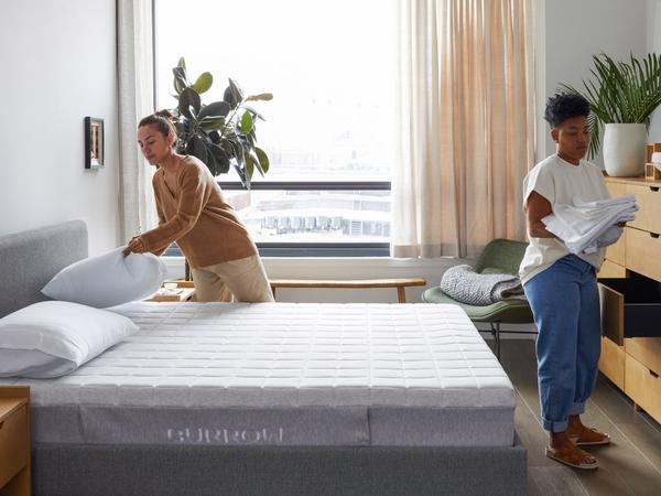 A couple making the bed over a Lyric mattress on an upholstered Chorus bed in gray