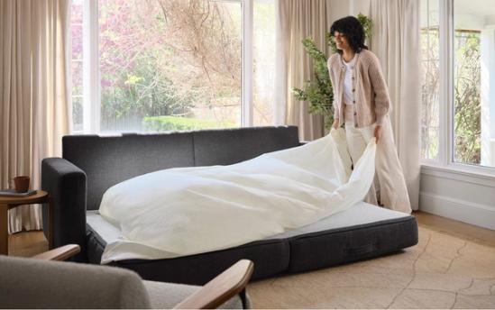 Woman setting up bedding on a charcoal span sleeper sofa