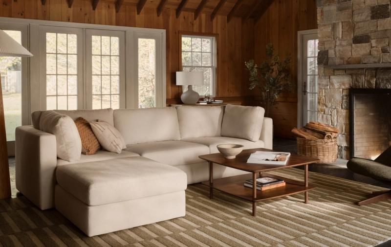 Union sectional with ottoman in ivory in a wood-paneled living room with a stone fireplace