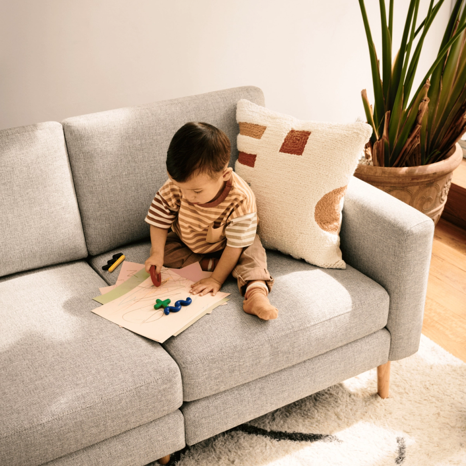 Toddler drawing with crayons on a light gray sofa