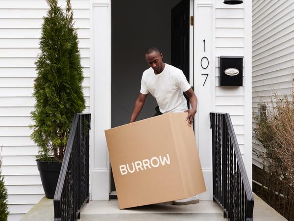 Man carrying in a Burrow box into his home from the front porch