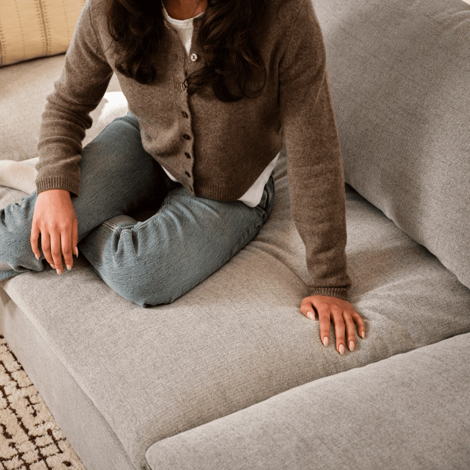 Woman sitting cross-legged on a light gray fabric sofa
