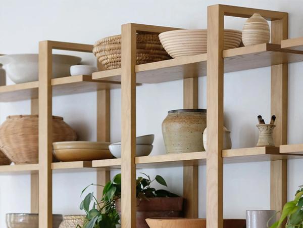 Wooden modular shelving unit displaying ceramic bowls, woven baskets, pottery, and small plants in geometric compartments