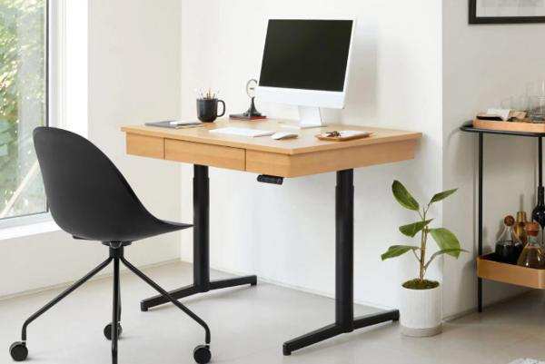 Modern home office with wooden standing desk, black swivel chair, computer monitor, and small plant