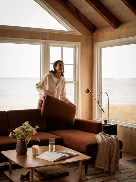 Woman lifting a reversible back cushion off a brown Nomad sectional by the window