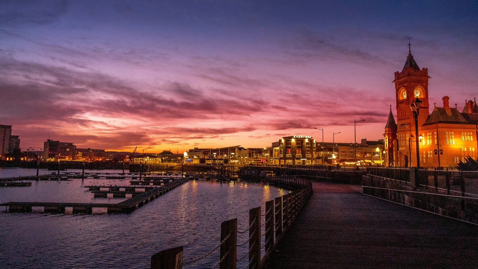 Cardiff Bay at dusk, with the illuminated Pierhead Building clock tower on the right and Mermaid Quay across the water.