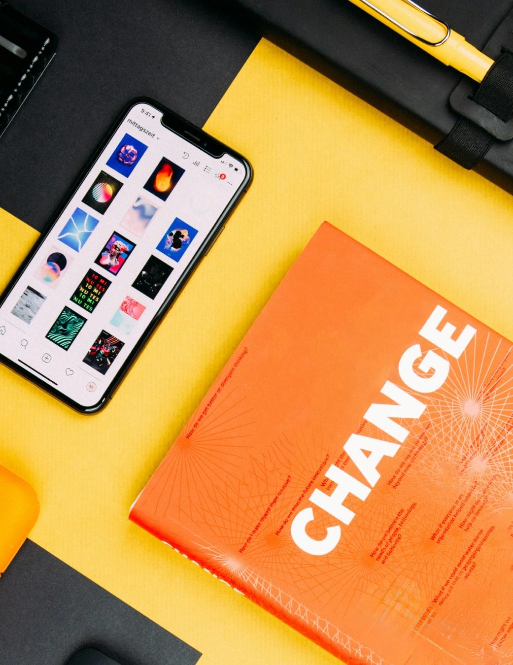 Flat lay of a phone showing an Instagram grid next to an orange magazine with bold "CHANGE" cover typography.