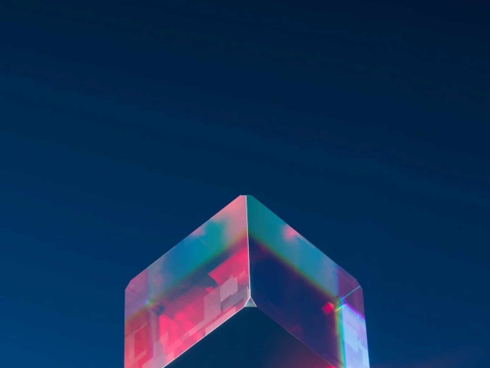Translucent glass cube refracting pink and red light against a deep blue background.
