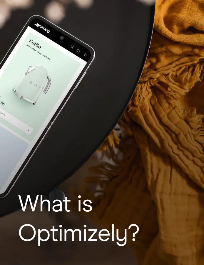 A smartphone displaying the Smeg website's kettle product page rests on a dark round table, next to a folded mustard-yellow textile. Text overlay reads: What is Optimizely?