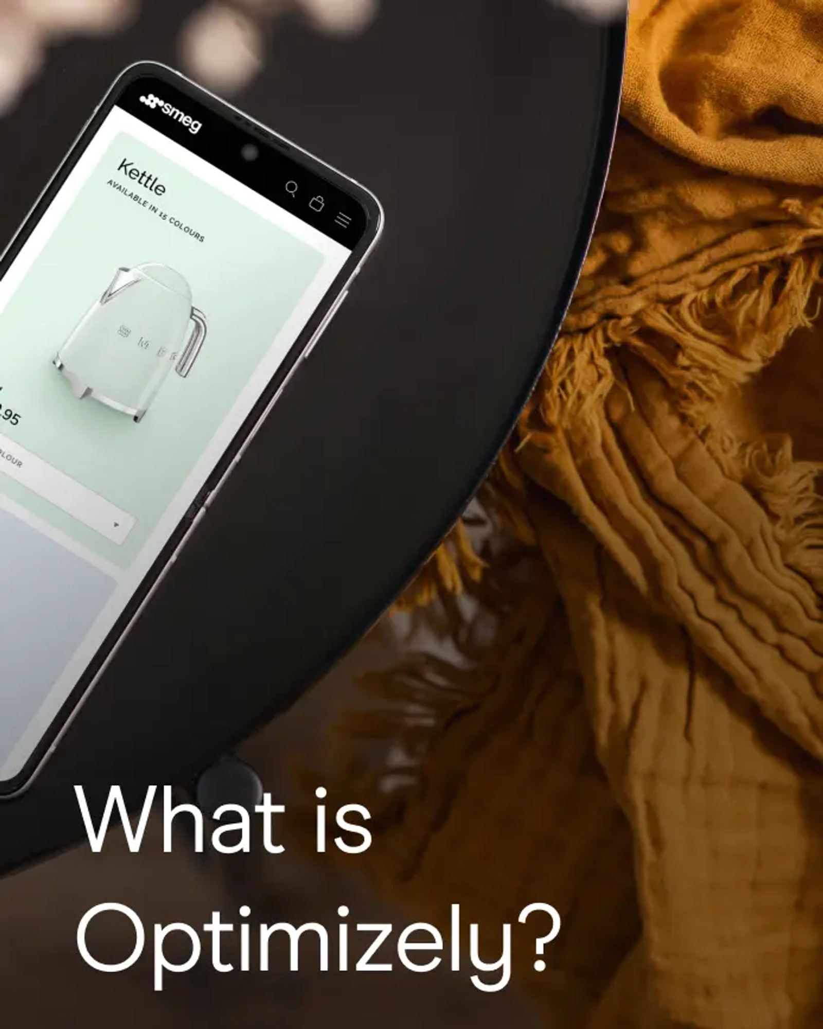 A smartphone displaying the Smeg website's kettle product page rests on a dark round table, next to a folded mustard-yellow textile. Text overlay reads: What is Optimizely?