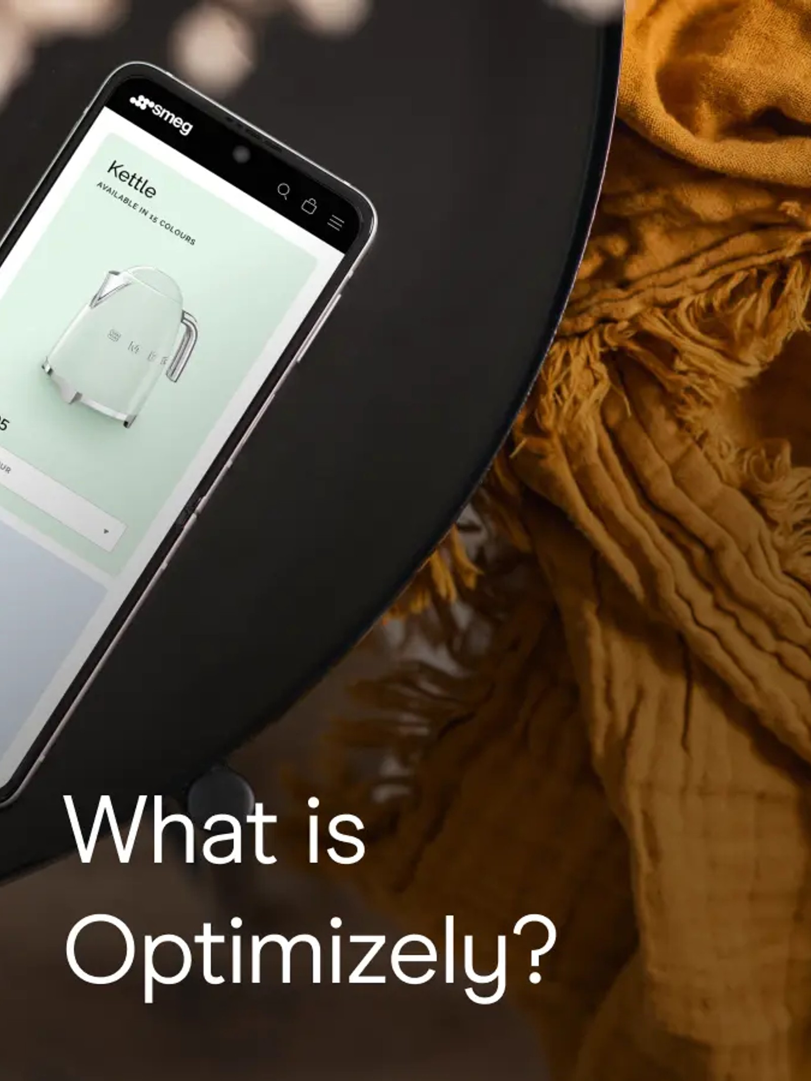 A smartphone displaying the Smeg website's kettle product page rests on a dark round table, next to a folded mustard-yellow textile. Text overlay reads: What is Optimizely?
