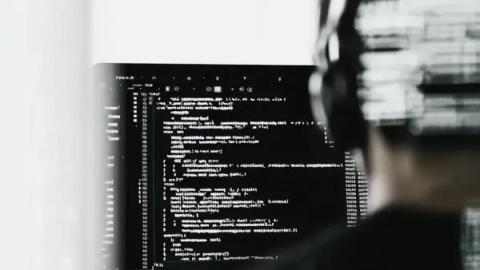 Close-up of code on a monitor with a developer working in the foreground.