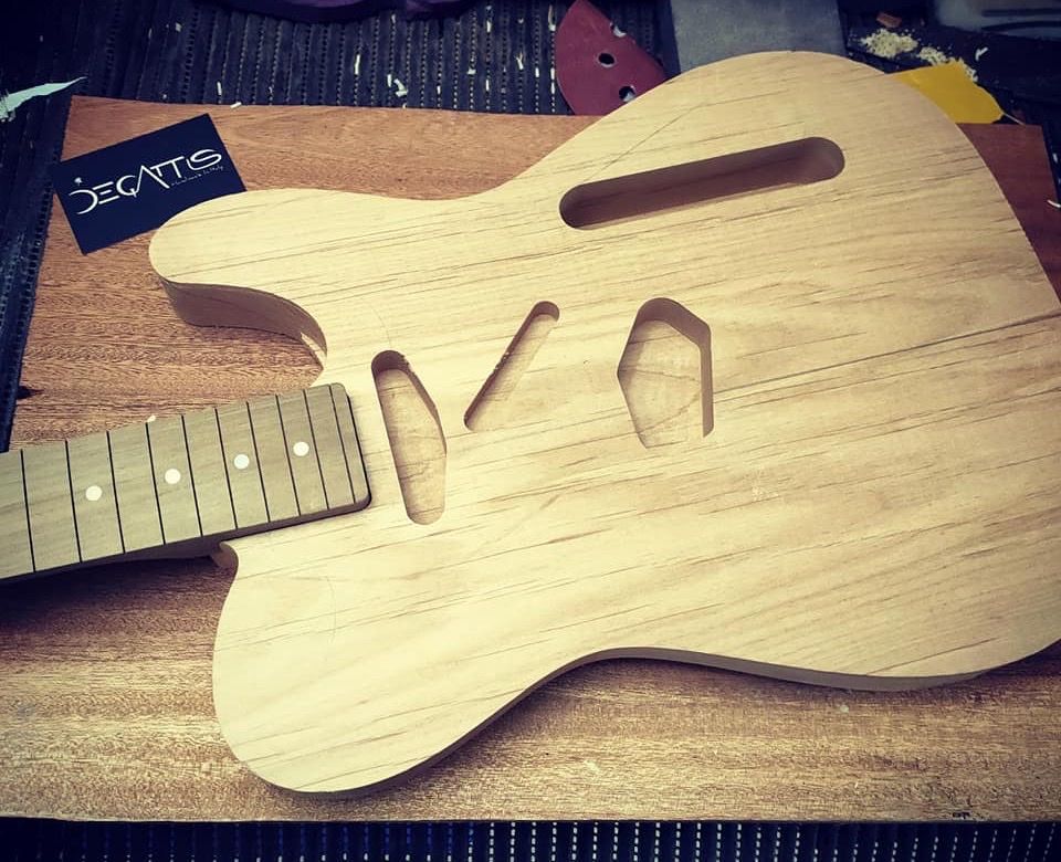 工房の作業台の上、削り出したばかりで無塗装の Thinline のボディ。横に指板が置かれている