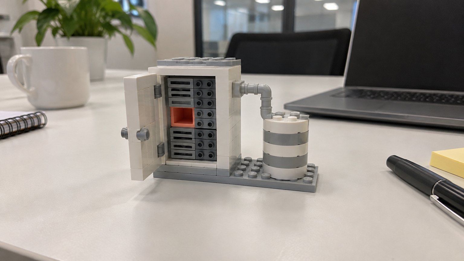 Toy-brick server cabinet with one coral-pink empty slot, on an office meeting table