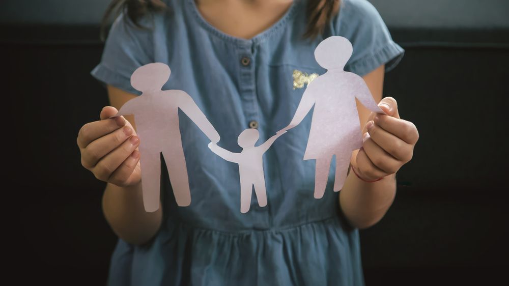 Paper cut-out figures of a family held in a pair of cupped hands