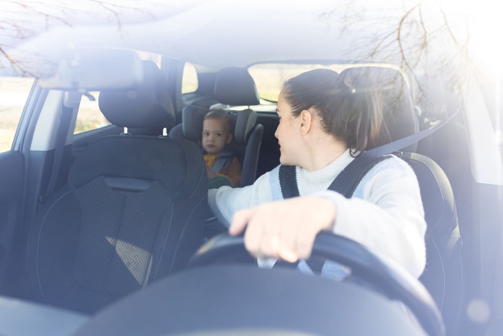 A driver at the wheel of a car with a child seated behind