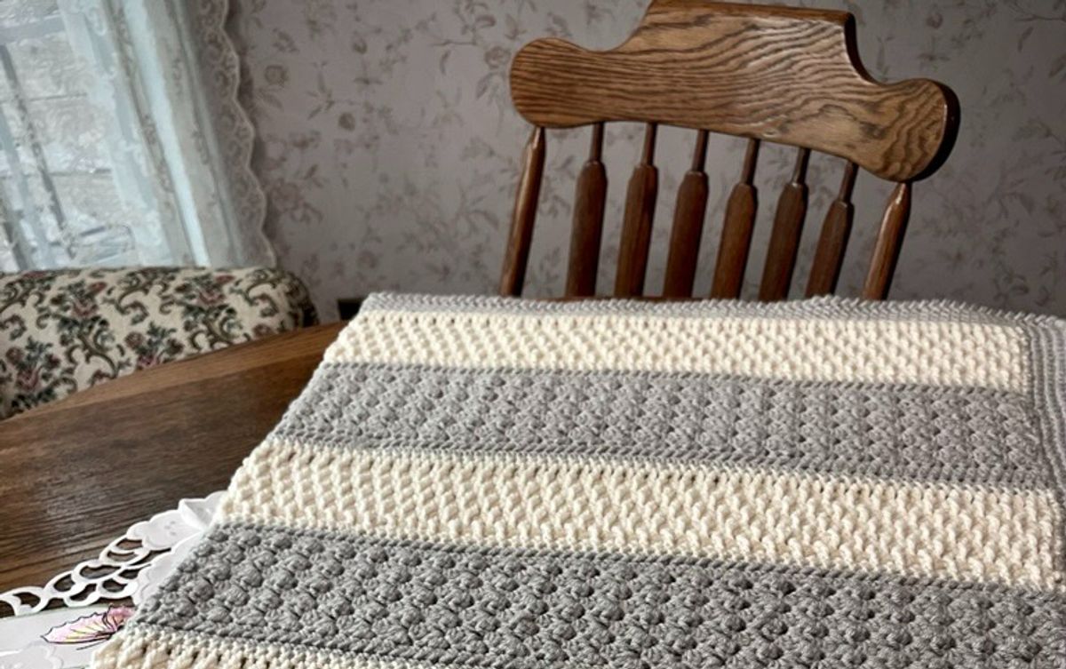 A cream and tan crochet scarf pinned out to dry on a gridded cutting mat, showing its scalloped edge