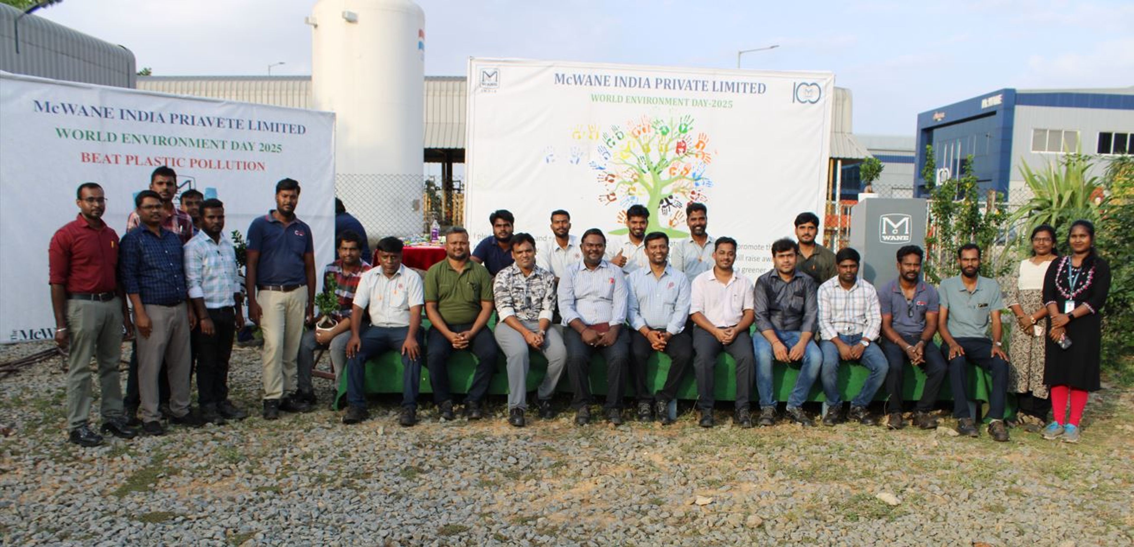 A group of people pose outdoors in front of banners reading “World Environment Day 2023” and “Beat Plastic Pollution” at McWane India Private Limited. Some are seated, others stand behind them, with greenery and buildings visible.