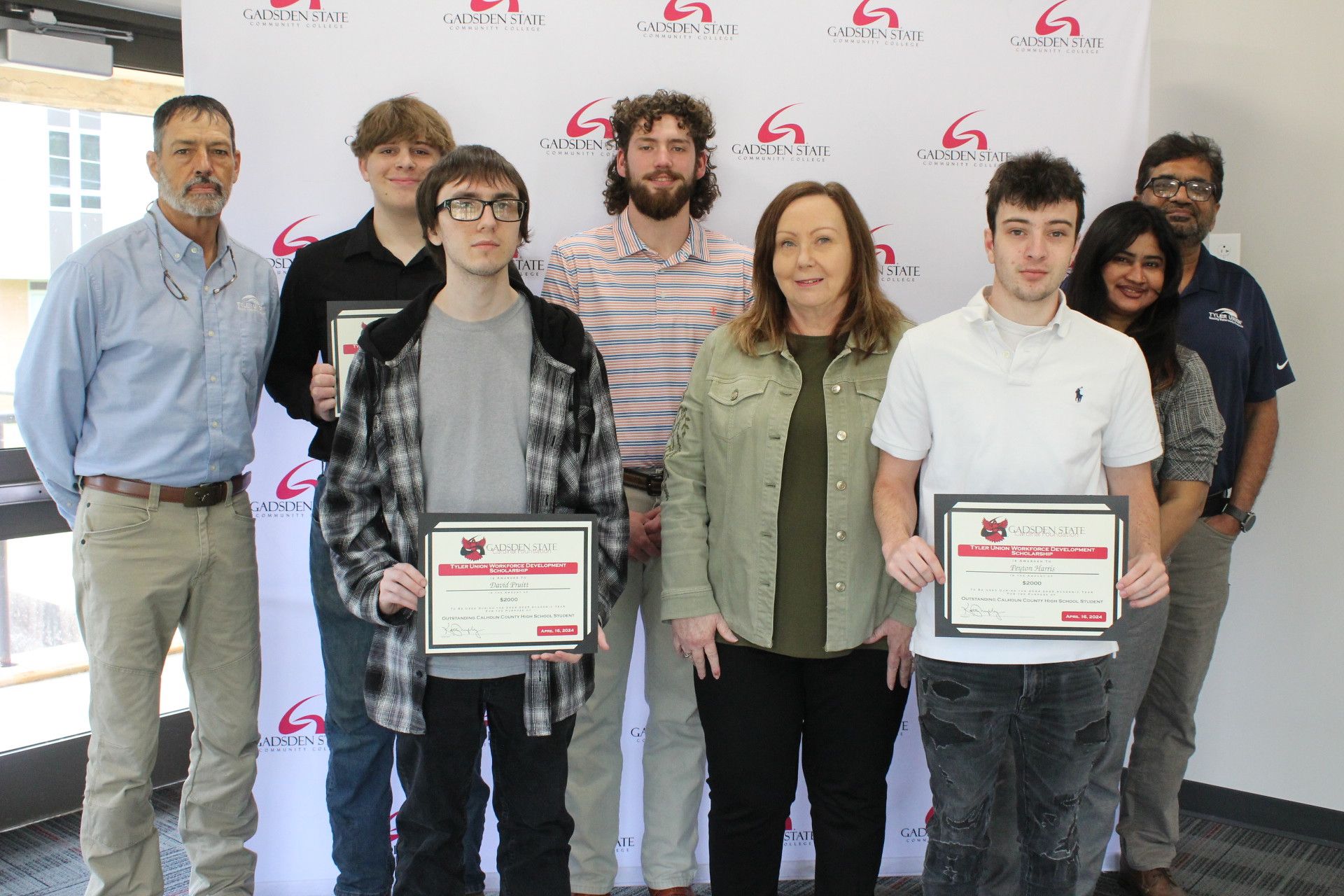 Eight people stand indoors, three holding certificates, in front of a backdrop with the “Garden State” logo. The group includes both men and women, all smiling and facing the camera.