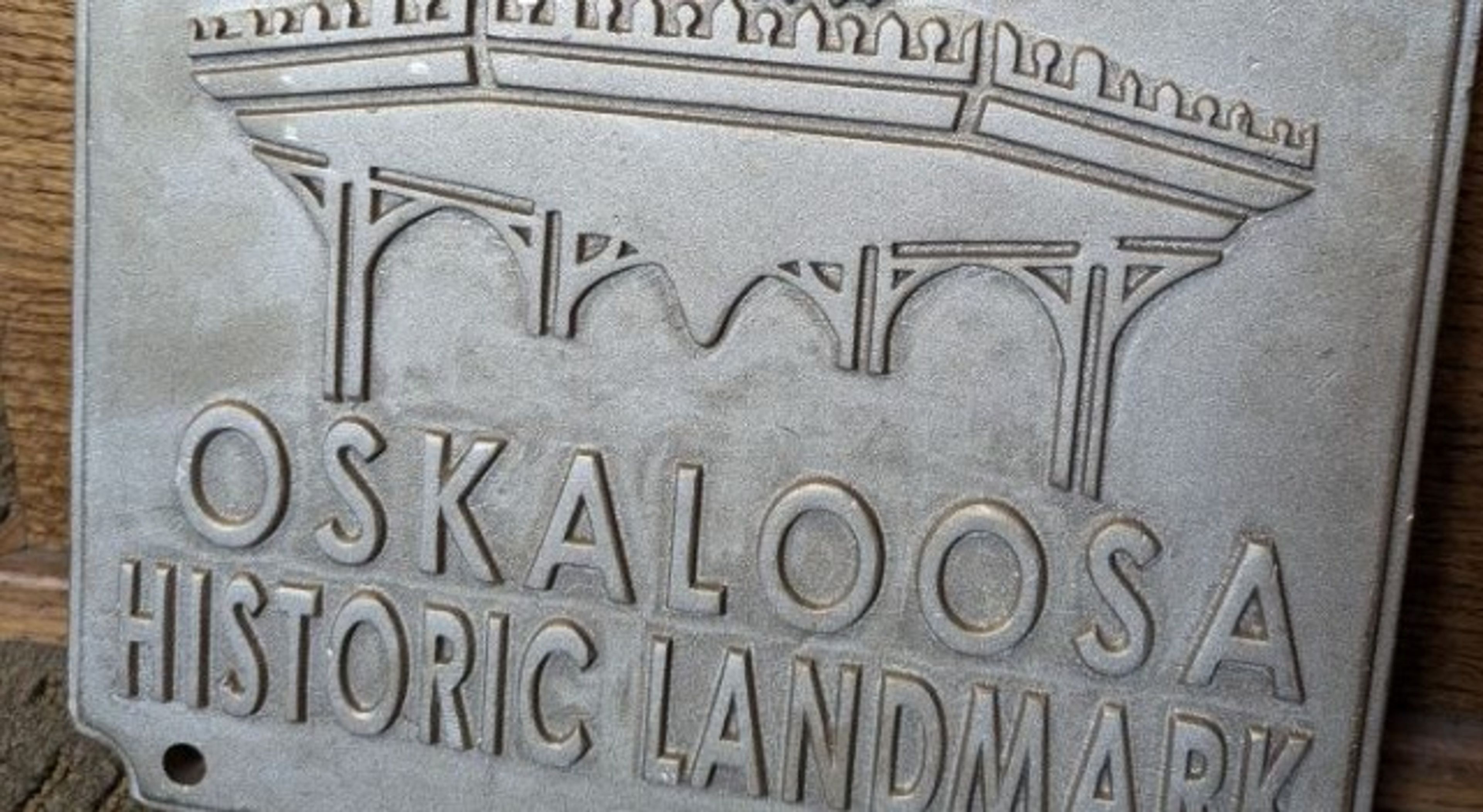 A metal plaque reads “Oskaloosa Historic Landmark” with an engraved image of an arched structure above the text.