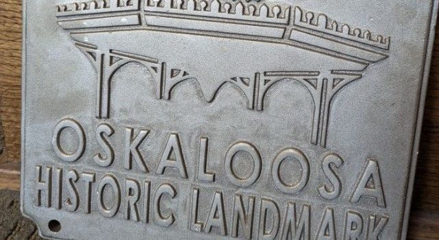 A metal plaque reads “Oskaloosa Historic Landmark” with an engraved image of an arched structure above the text.