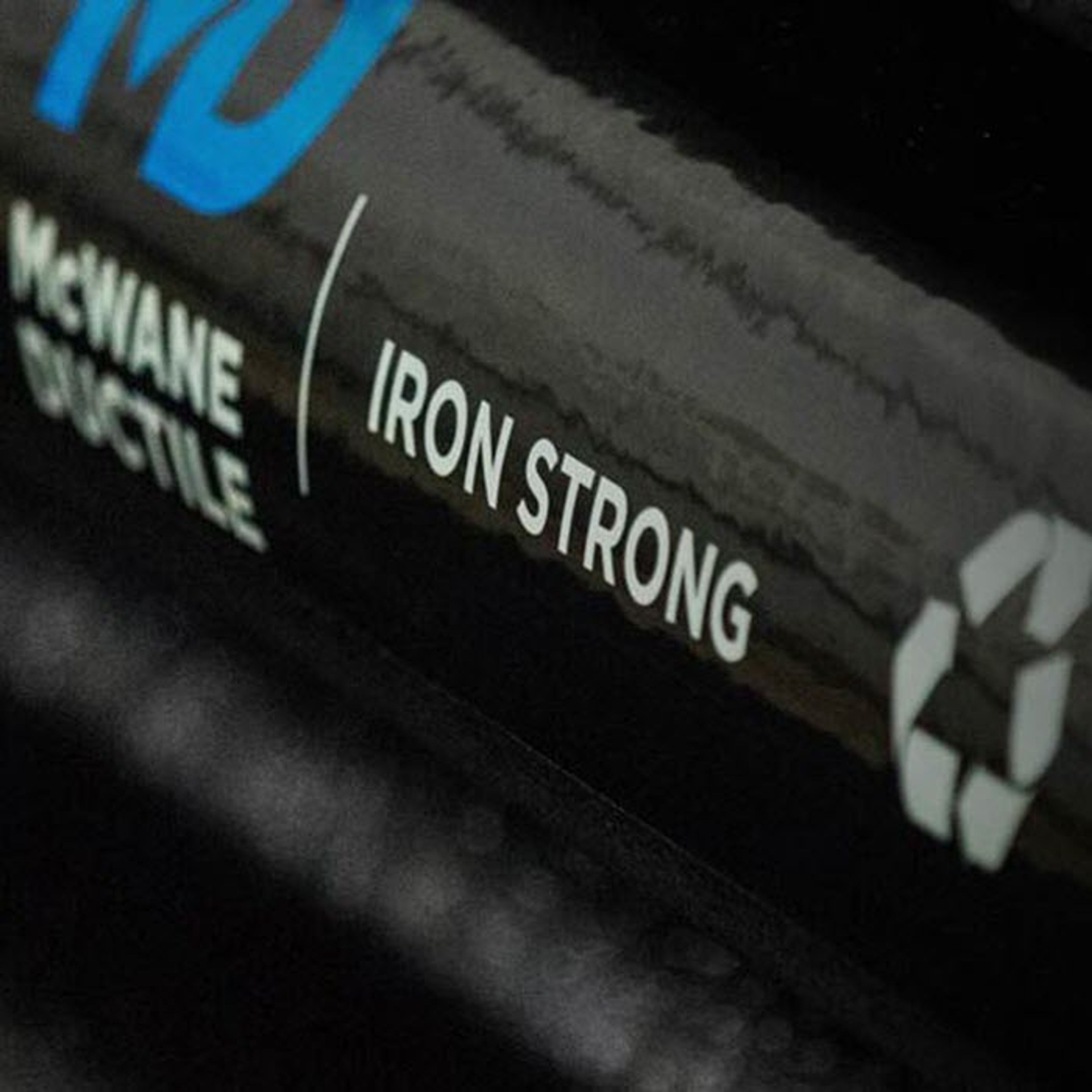 Close-up of a black pipe with the words “McWane Ductile | IRON STRONG” and a recycling symbol printed in white on its surface. The text is clearly visible and stands out against the dark background.