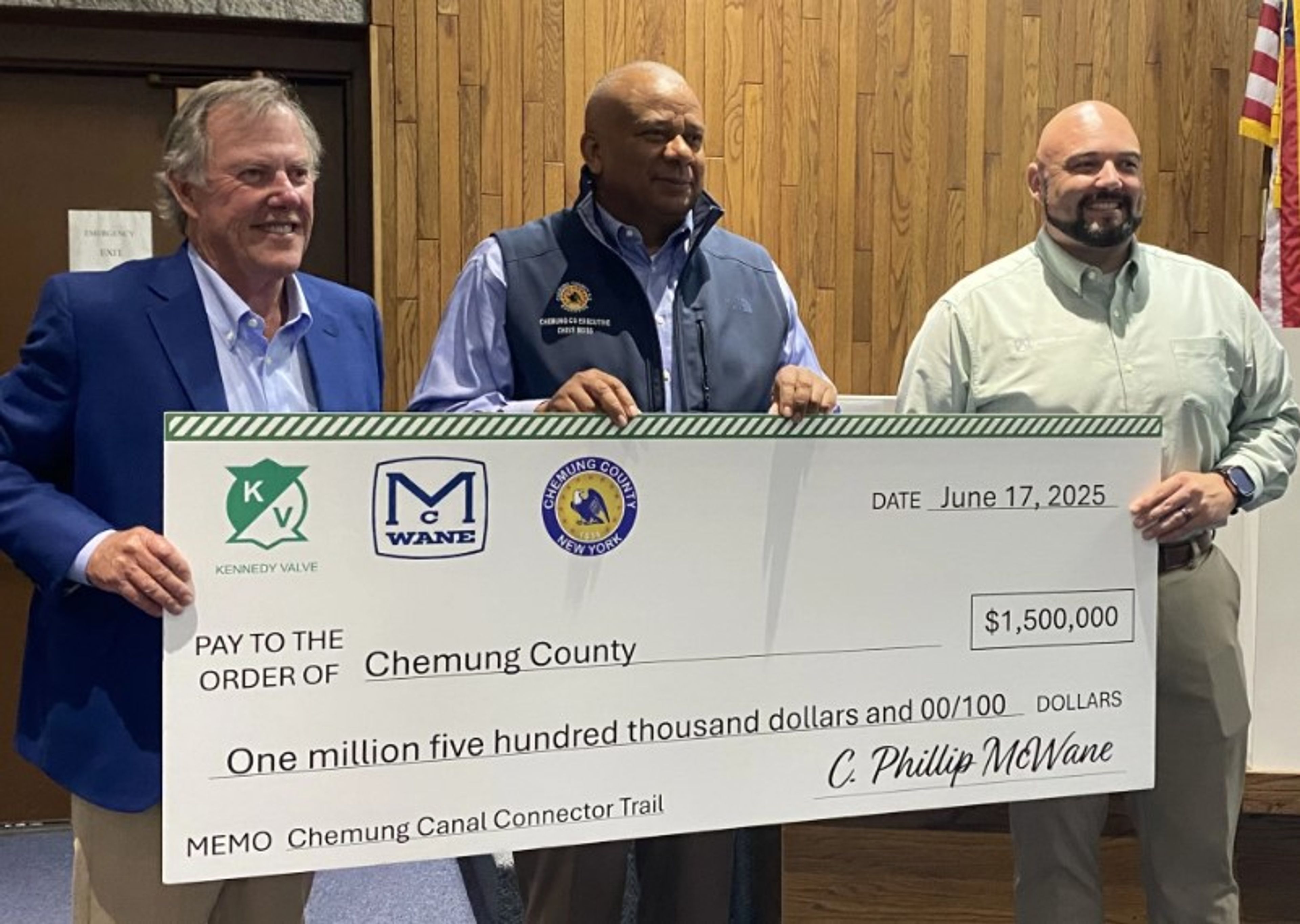 Three men smiling and holding a large ceremonial check for $1,500,000 made out to Chemung County, dated June 17, 2025, for the Chemung Canal Connector Trail.
