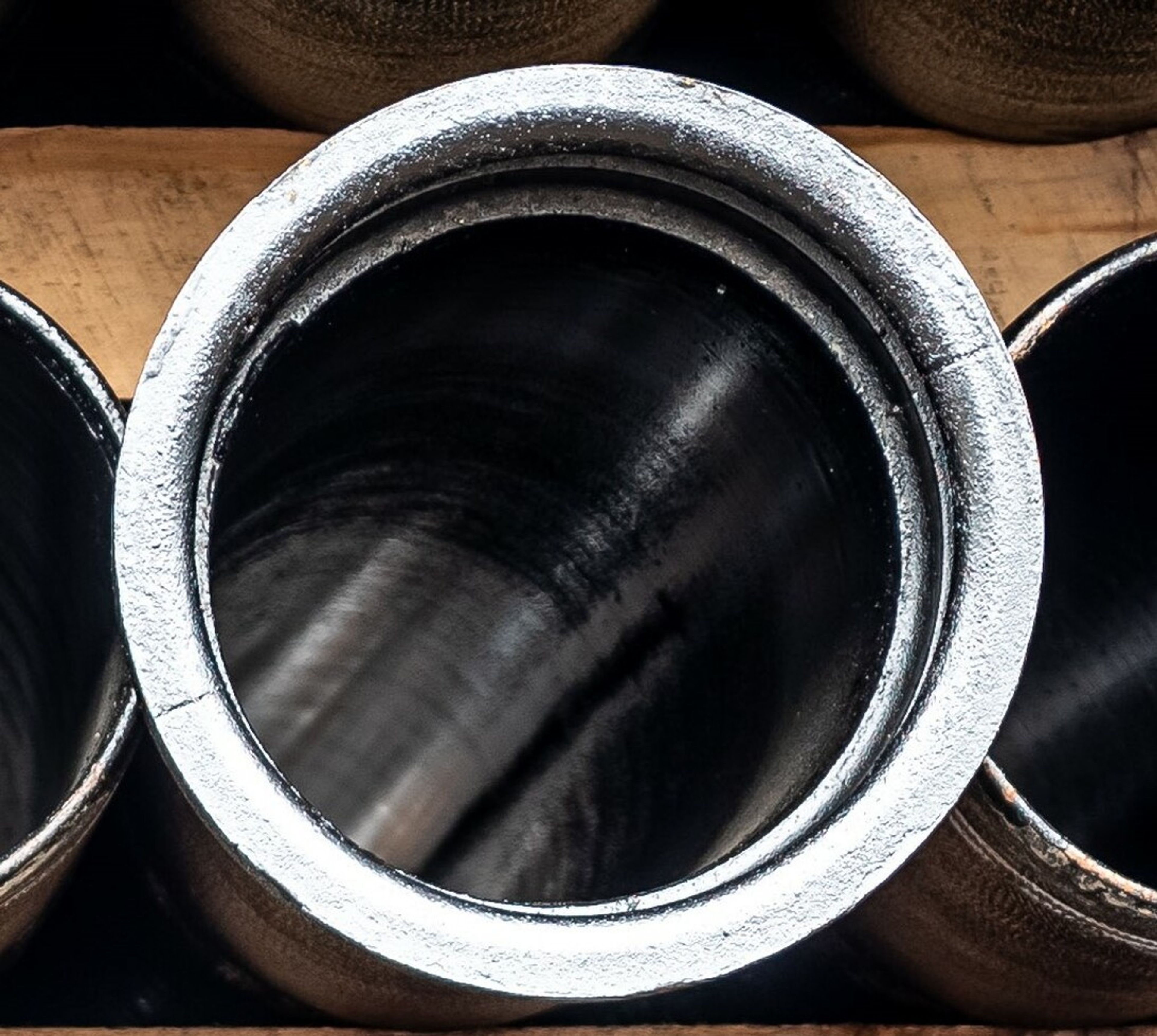 A close-up view of a shiny, cylindrical metal pipe with a silver rim, placed vertically on a wooden surface.