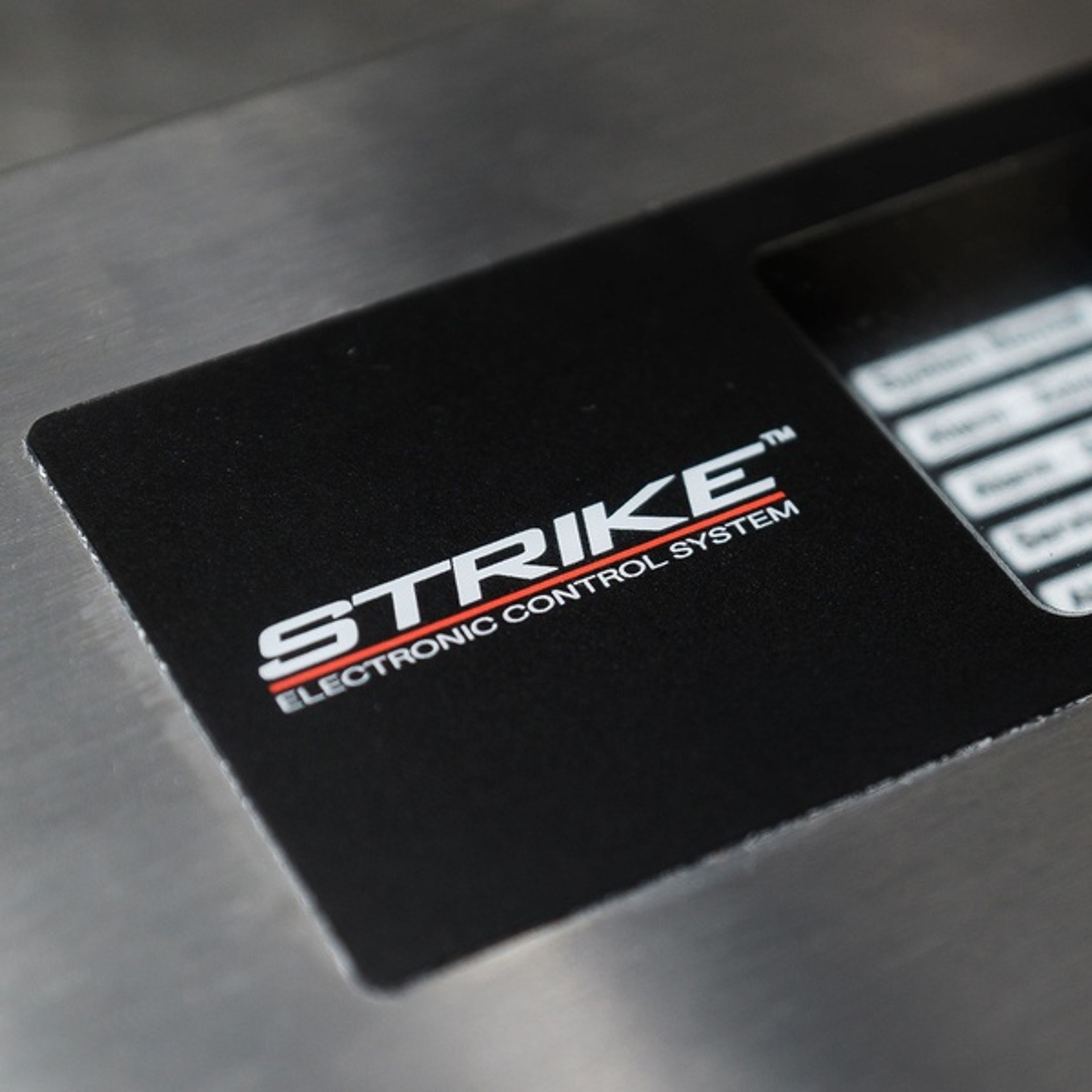 Close-up of a black panel with the white text “STRIKE Electronic Control System” in bold letters, part of a metal device.