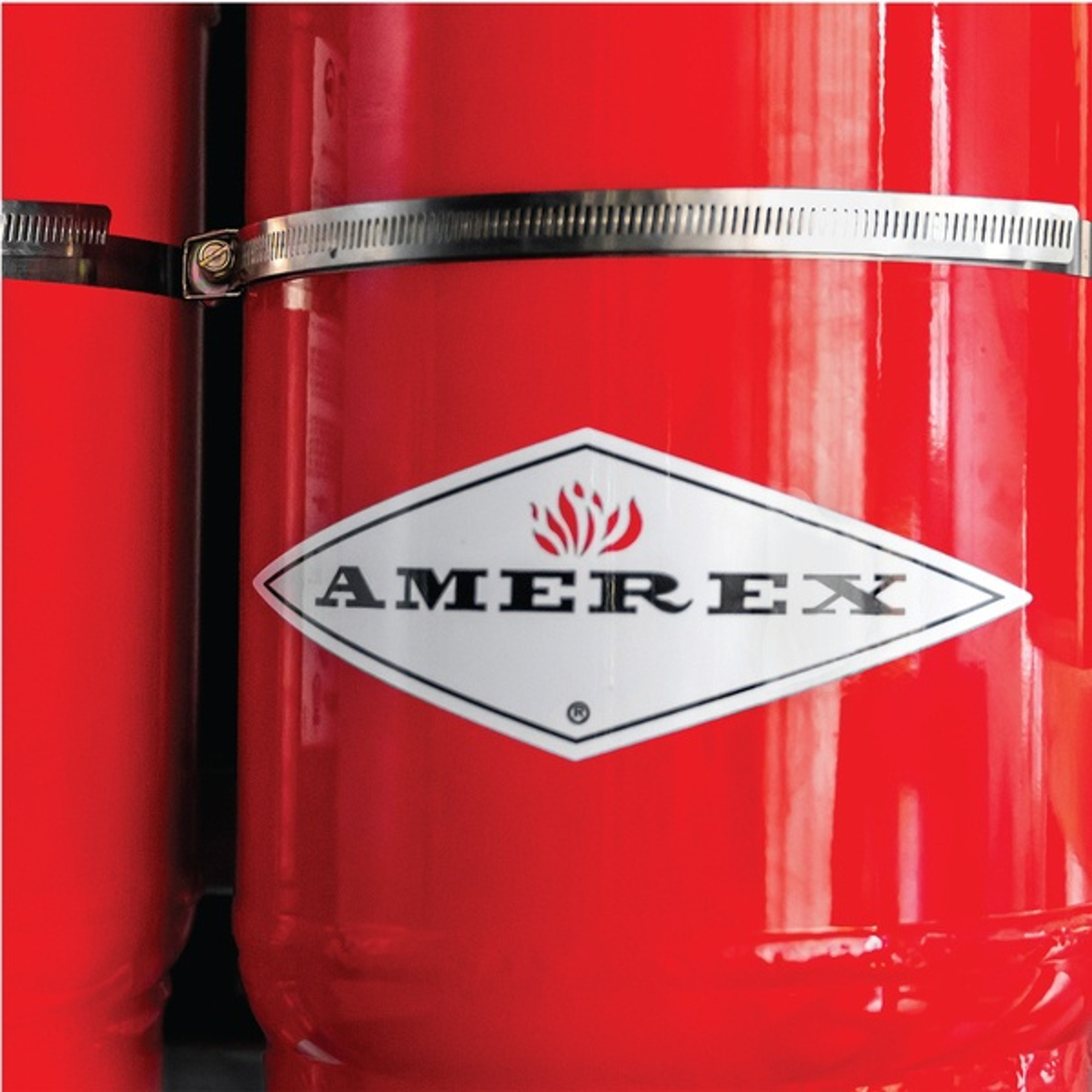 Close-up of a red fire extinguisher with a metal strap and a diamond-shaped “Amerex” logo featuring a flame symbol in the center.