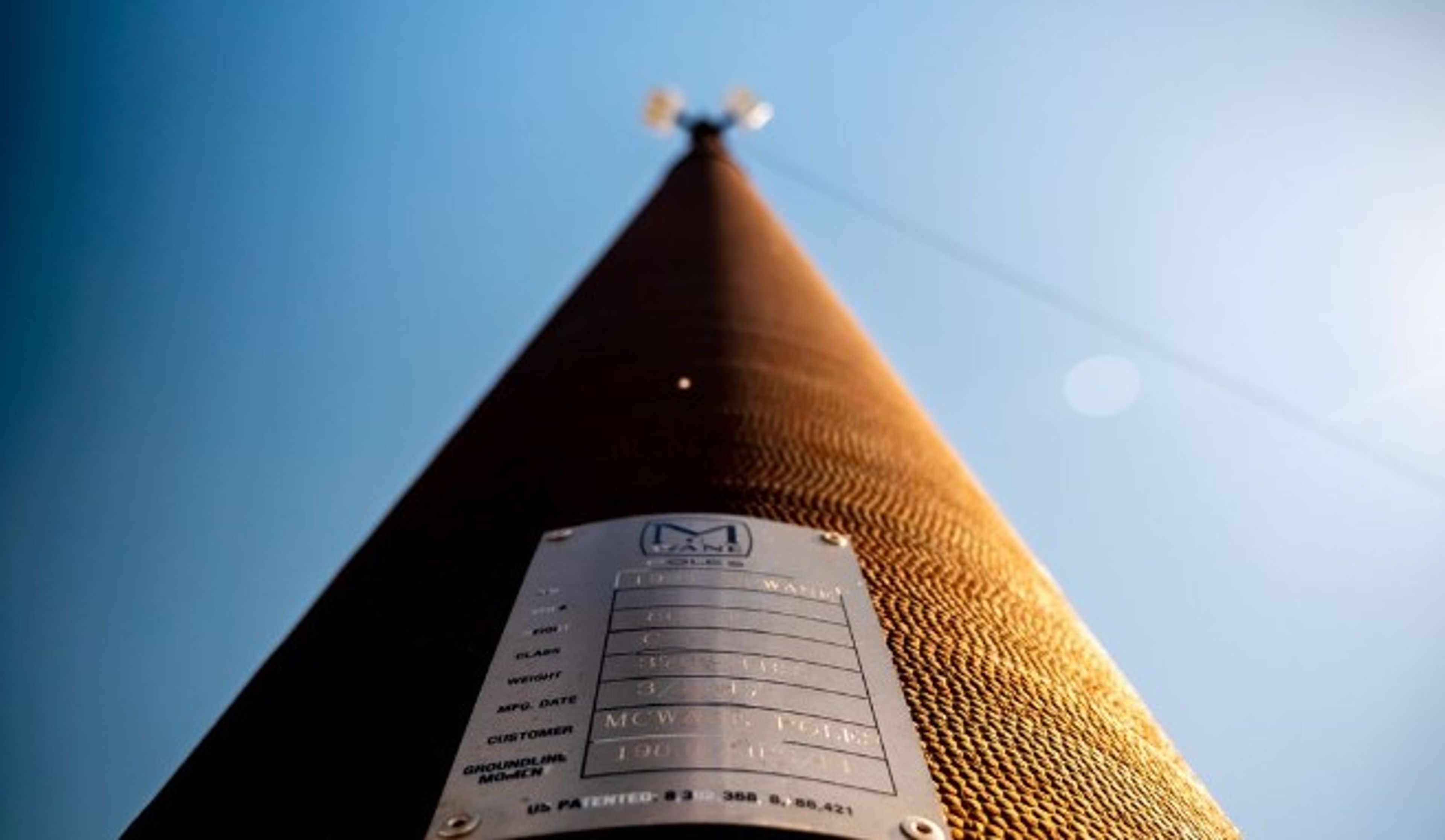 Low-angle view of a tall, textured utility pole with a metal information plate in focus near the base and a clear blue sky in the background.