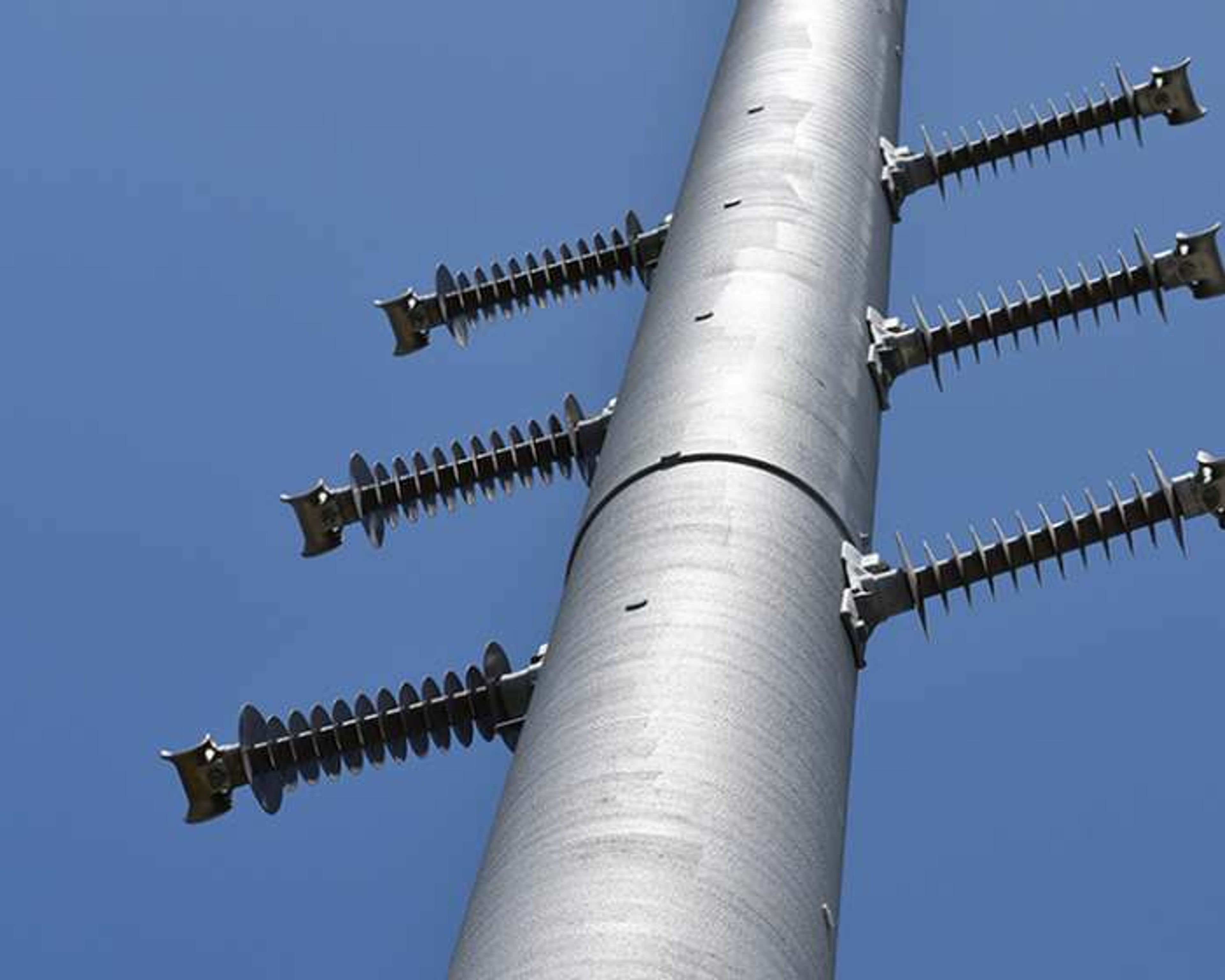 Close-up view of a tall utility pole with multiple insulators extending horizontally, set against a clear blue sky.