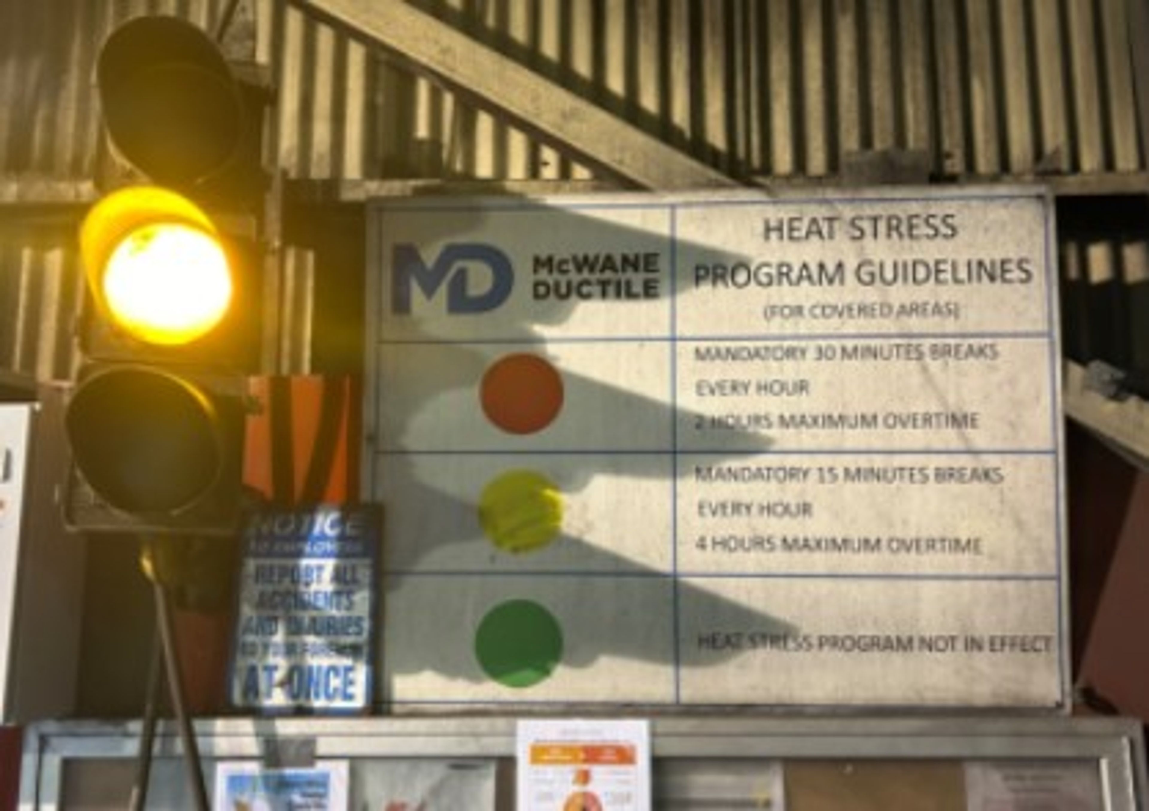A caution light shows yellow beside a McWane Ductile heat stress guideline sign detailing break requirements based on colored signal lights: red, yellow, or green.