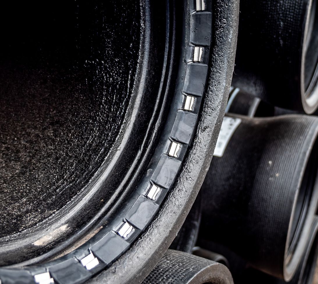 Close-up of large black industrial pipes stacked together, showing a detailed view of the smooth inner surface and reinforced metal rings or bands along the pipe edge.