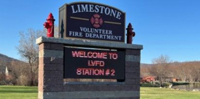 A stone sign reads “Limestone Volunteer Fire Department” with an electronic display below saying “WELCOME TO LVFD STATION #2.” The sign is outdoors with grass and trees in the background.