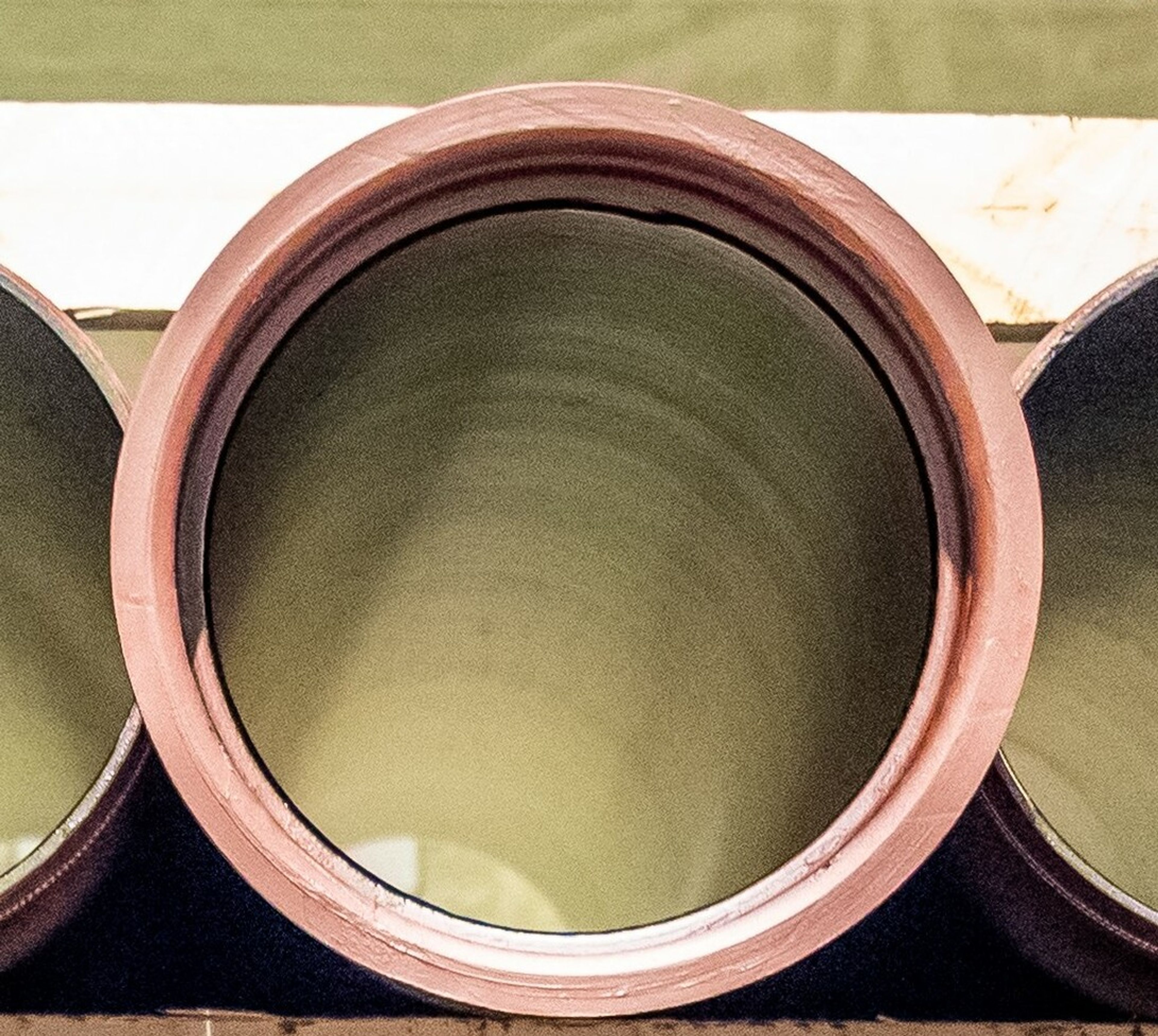 A large black pipe runs horizontally behind white metal framework with diagonal supports; blue sky and trees are reflected in a background surface, possibly water or glass.